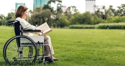Una mujer con discapacidad en silla de ruedas, leyendo en un parque