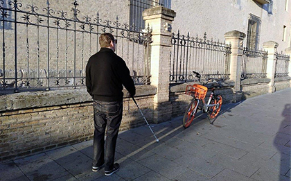 persona con bastón andando por acera con una bicicleta a un lado con riesgo para su seguridad