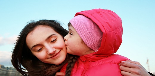 Una pequeña niña besa a su mamá que ríe con alegría
