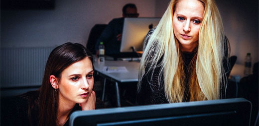 Trabajadoras en una oficina, donde se cumple la conciliación de la vida familiar y laboral, mirando algo en un ordenador