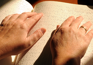 Una manos de una persona con discapacidad leyendo un libro en braille, versus minusvalía