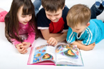 3 niños tumbados en suelo leyendo un cuento - Sistema educativo: infantil