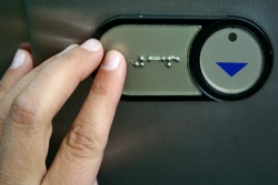 mano pulsando botón en braille de ascensor