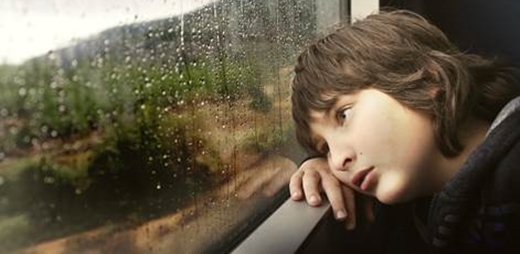 Niño con discapacidad sensorial confinado mirando un paisaje lluvioso a través de la ventana