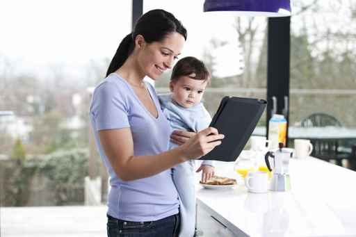  Una mamá joven con su hijo en brazos y mirando una tablet sonriendo como marca la guía de pensamiento positivo