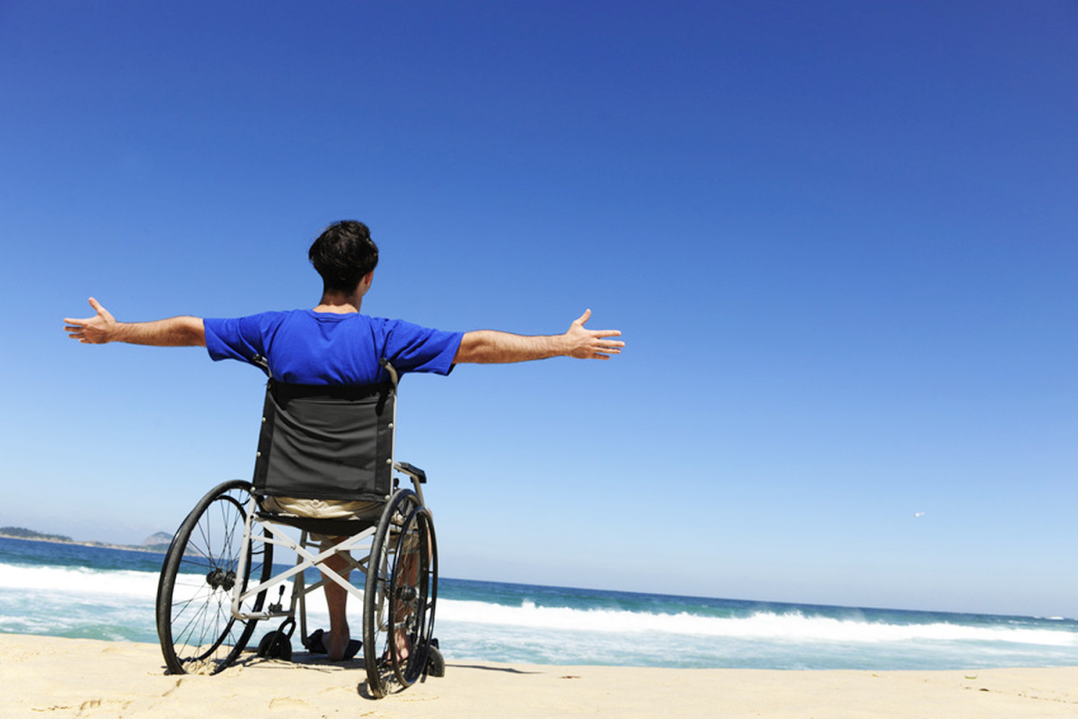 Un joven en silla de ruedas en la playa con las manos en alto en señal e alegría, ejemplo de la guía de pensamiento positivo 