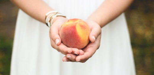 Mujer mostrando melocotón, para la hernia de hiato se recomienda alimentación saludable