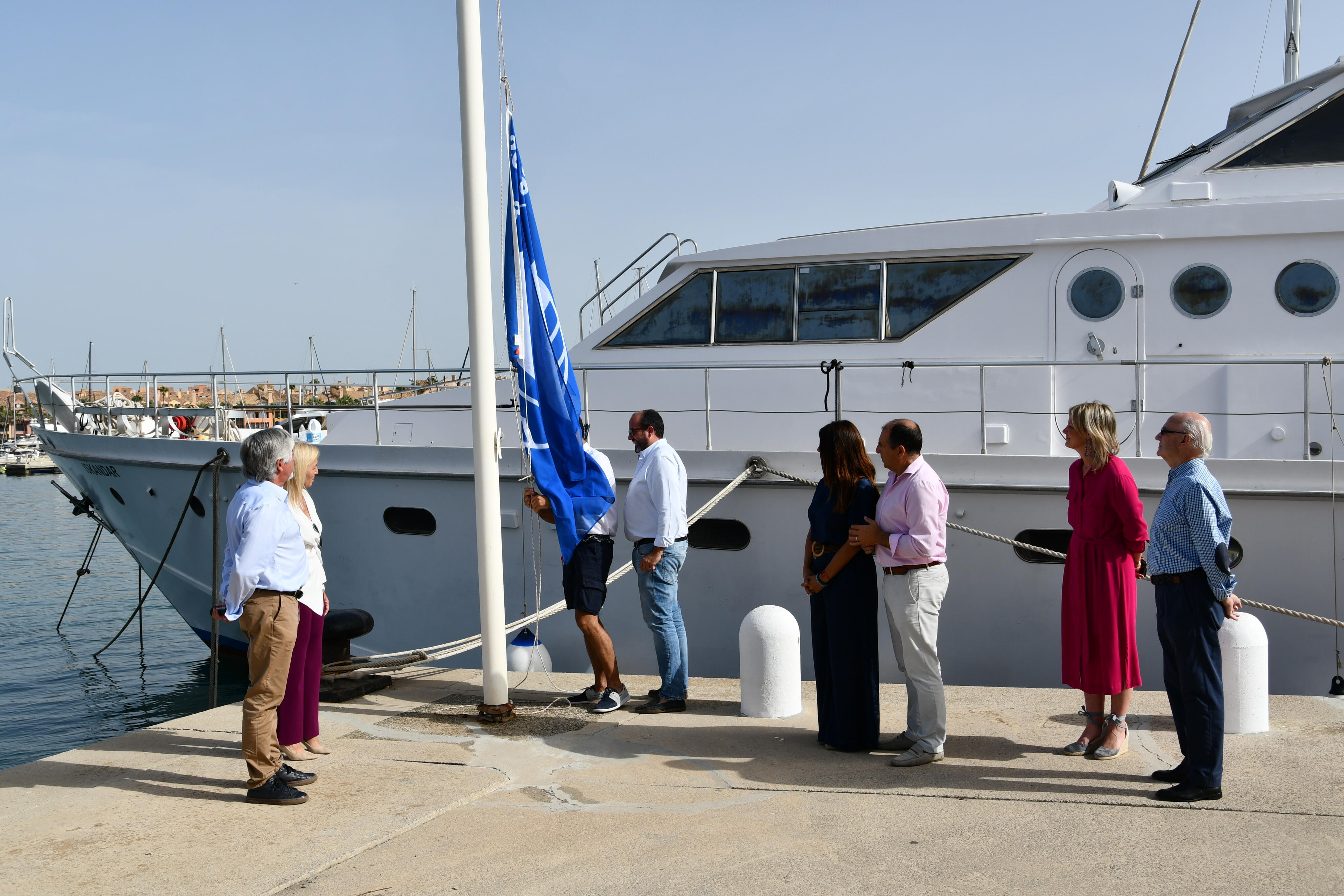 Personas izando la bandera azul en el Puerto de Sotogrande