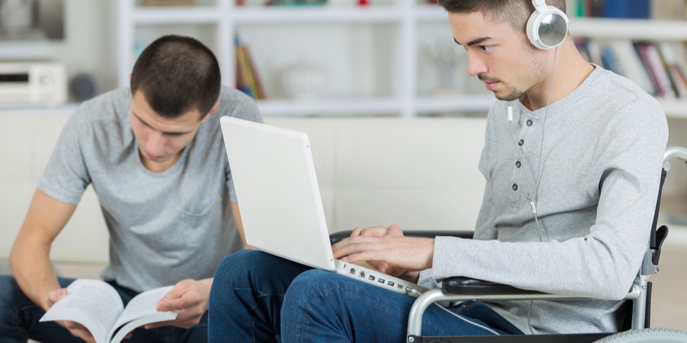 Dos chicos, uno sin discapacidad y con un libro y otro con discapacidad y con el ordenador estudiando en una biblioteca