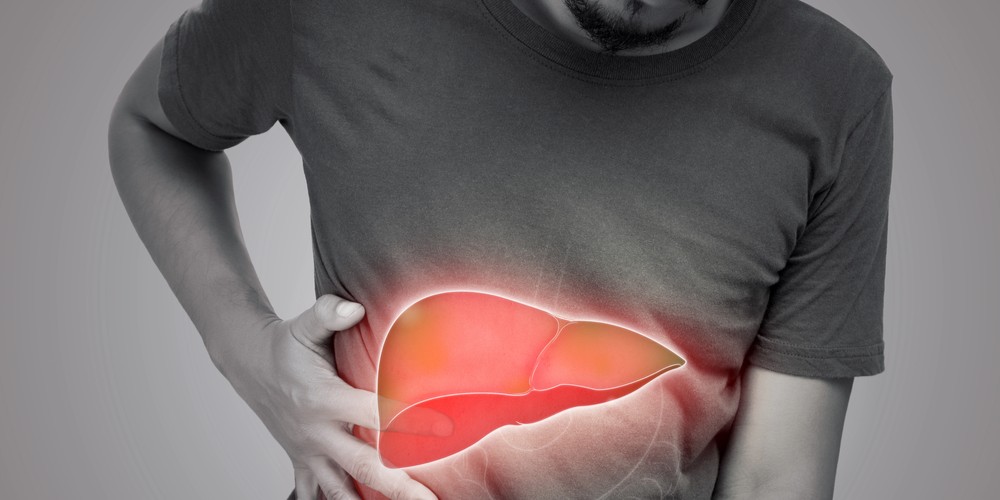 Persona sujetándose el lado derecho del abdomen con una mano mientras una ilustración semitransparente del hígado, destacada en tonos rojizos y anaranjados, aparece superpuesta sobre la zona. La imagen simboliza dolor, inflamación o enfermedad hepática sobre un fondo gris neutro.