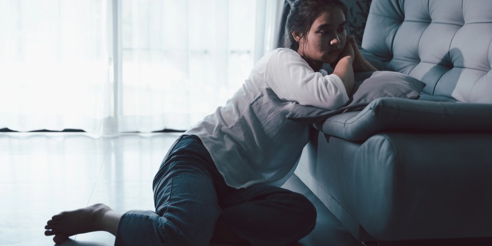 Persona tirada en el suelo, apoyada en el sofa, reflejando fatiga corporal y mental