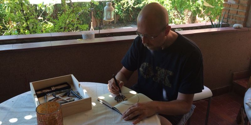 Jesús Galiana en una mesa en del patio dibujando a tinta en un libro