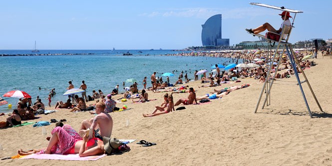 PLaya de la Barceloneta con gente en la arena y bañándose, al fondo de ve el hotel W Barcelona y también un socorrista