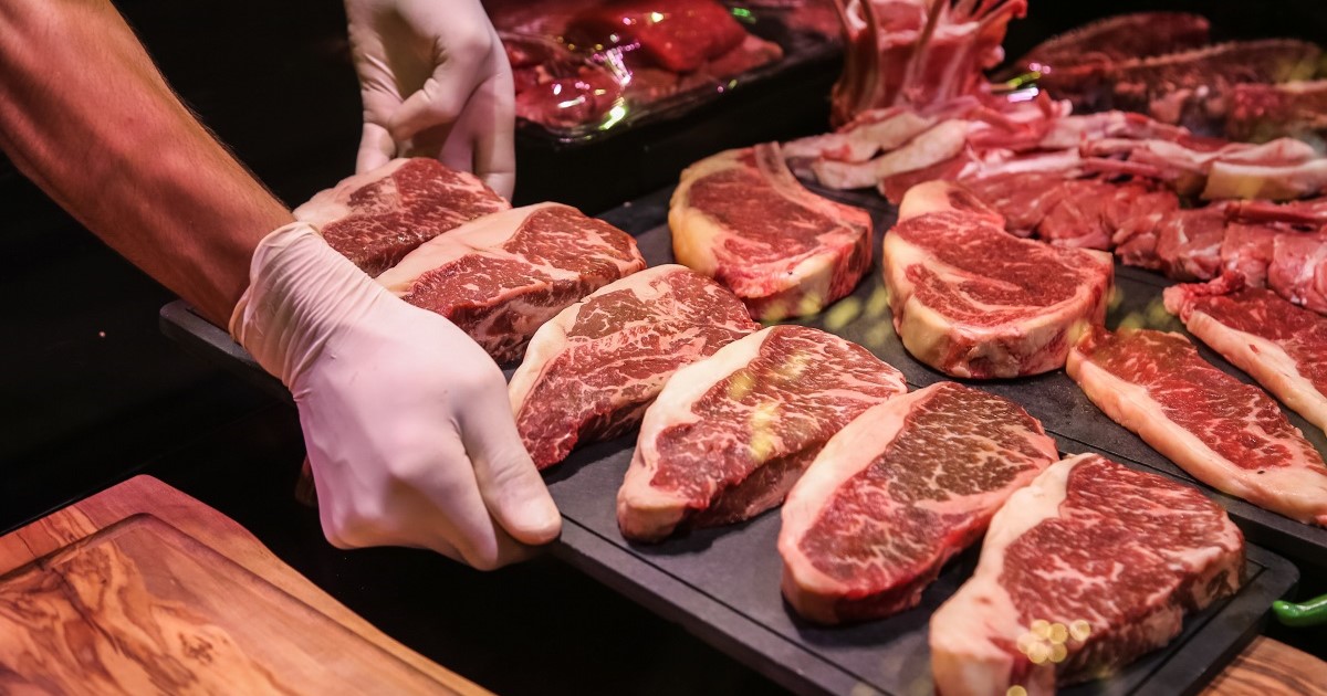 carnicero colocando en una bandeja varios filetes de carne roja