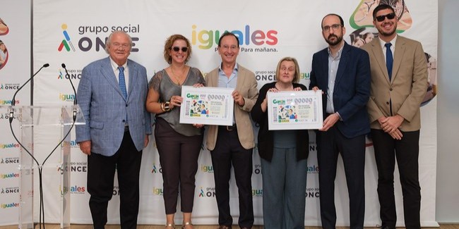 6 personas de la once sosteniendo dos cupones conmemorativos y posando a cámara delante de un cartel promocional de la ONCE