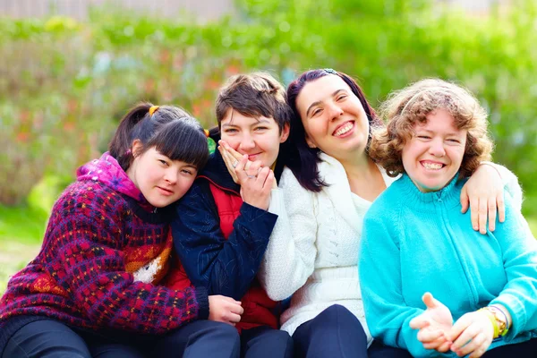 Grupo de cuatro personas sentadas al aire libre en una zona verde. Las personas aparecen juntas y en actitud cercana, vestidas con ropa de distintos colores, en un entorno natural con vegetación desenfocada al fondo. La imagen transmite convivencia, participación e inclusión social de personas con discapacidad intelectual.