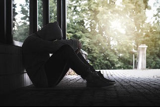 Una persona joven sentado en el suelo del patio del colegio y la cabeza entre las manos, otro síntoma de que sufre depresión