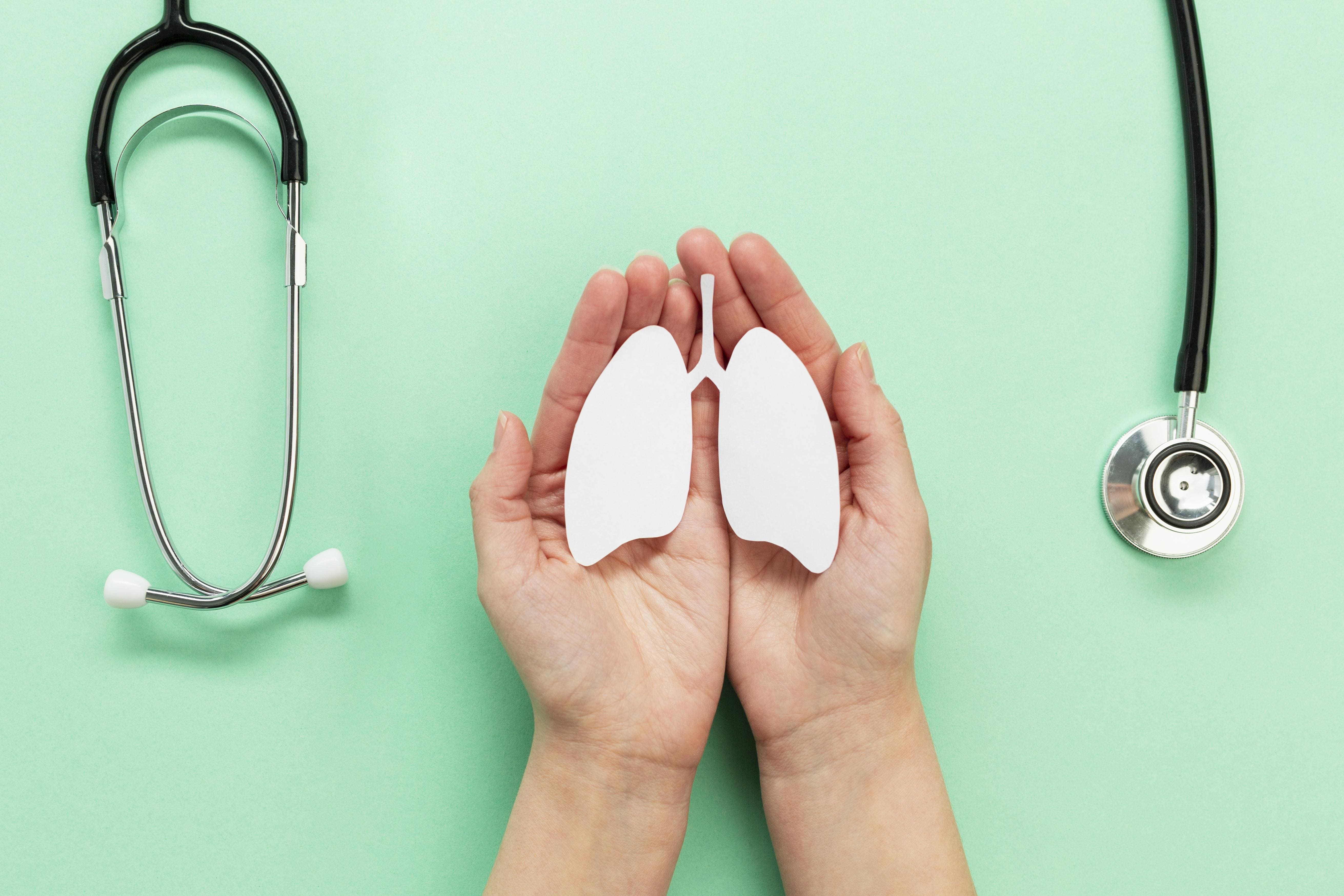 Manos sosteniendo unos pulmones de papel y un estetoscopio