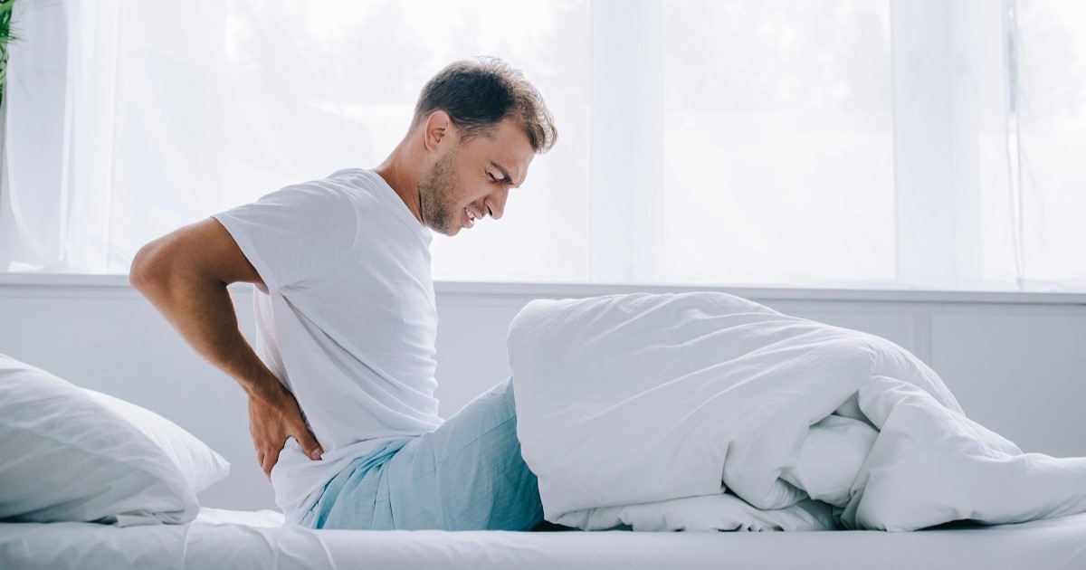 vista lateral de un hombre con pijama en la cama con dolor de espalda.