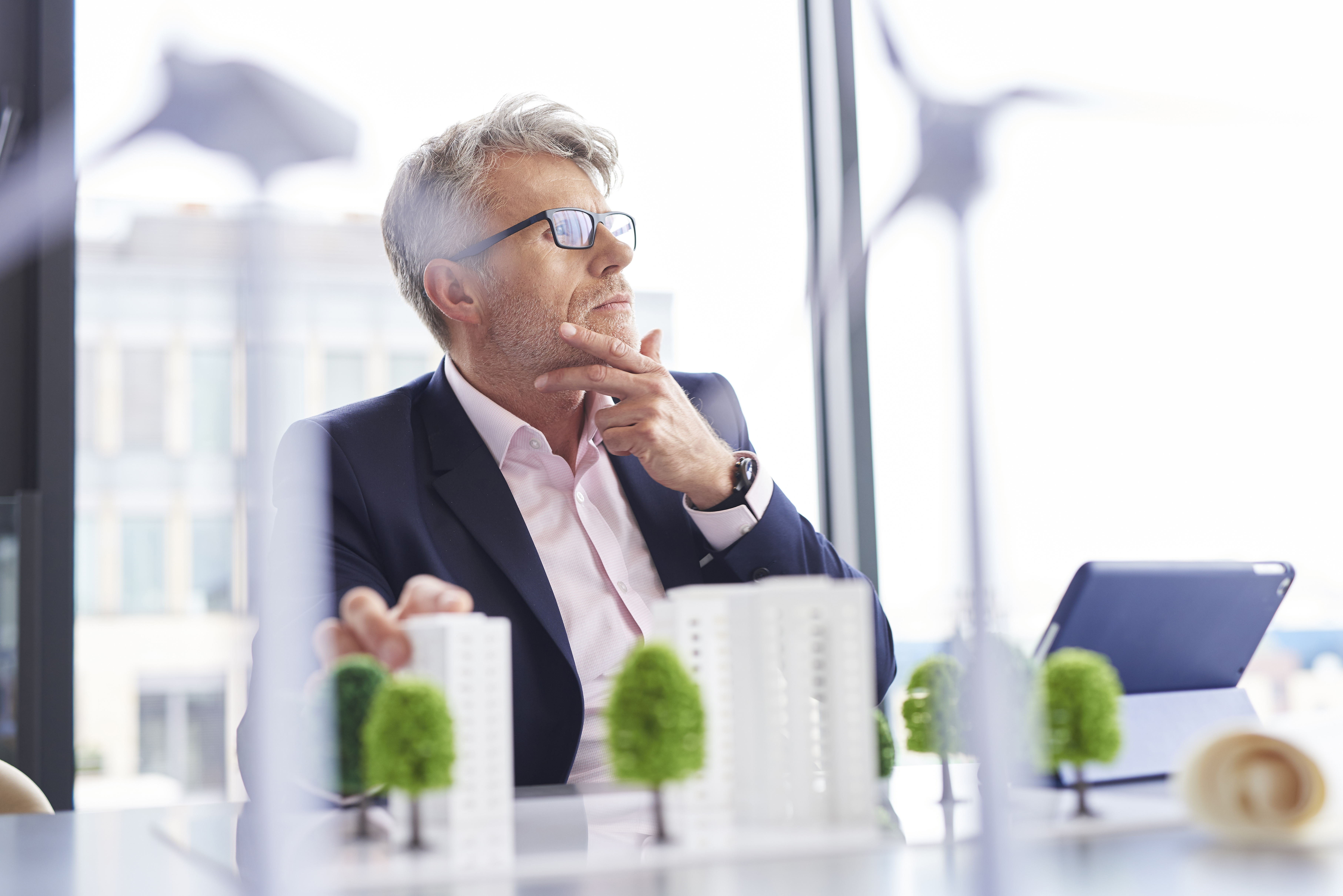 Hombre de negocios ocupado pensando en nuevas soluciones verdes. En la foto aparece el hombre junto a una maqueta de su empresa con árboles.