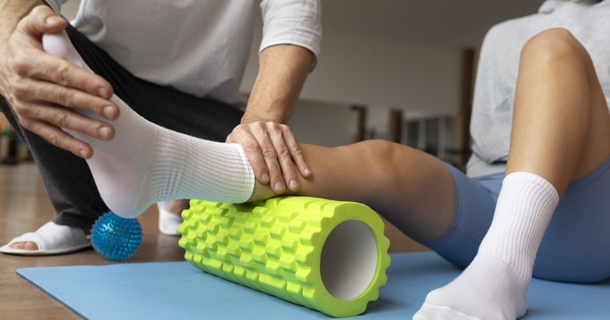 un hombre esta recibiendo rehabilitación, en el pie derecho, se encuentra tubado sobre una esterilla y un fisio le esta tocando el pie