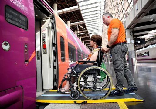 Una persona en silla de ruedas con ayuda de una persona subiendo a un tren.