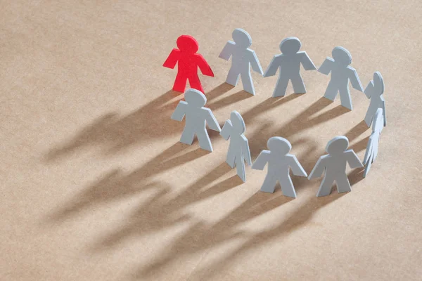 Recortes de papel con forma de persona, formando un circulo agarradas de la mano, una de las personas esta pintada de color rojo, representando diferencia frente al resto pintadas de gris. 