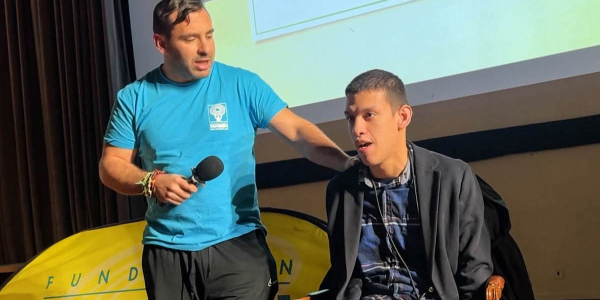 Kenjy en una ponencia subido al escenario con un hombre que le sujeta el micrófono.