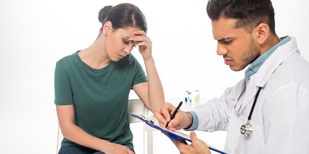 mujer con cara de tristeza al recibir sus resultados médicos del doctor que está a su lado
