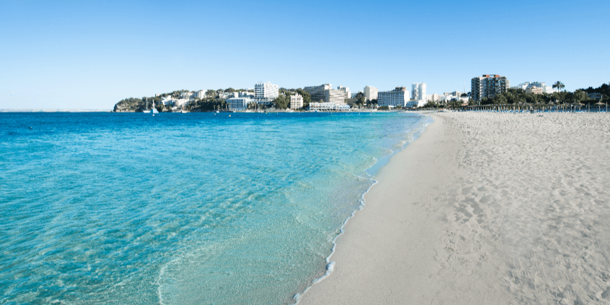 Playa de Palmanova con un agua cristalina, una arena muy fina y de color blanquecino, al fondo se pueden observar hoteles y apartamentos