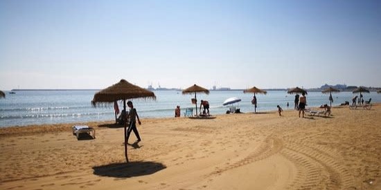 Playa de los Cárabos con las sombrillas puestas y gente paseando por la arena o en las tumbonas.