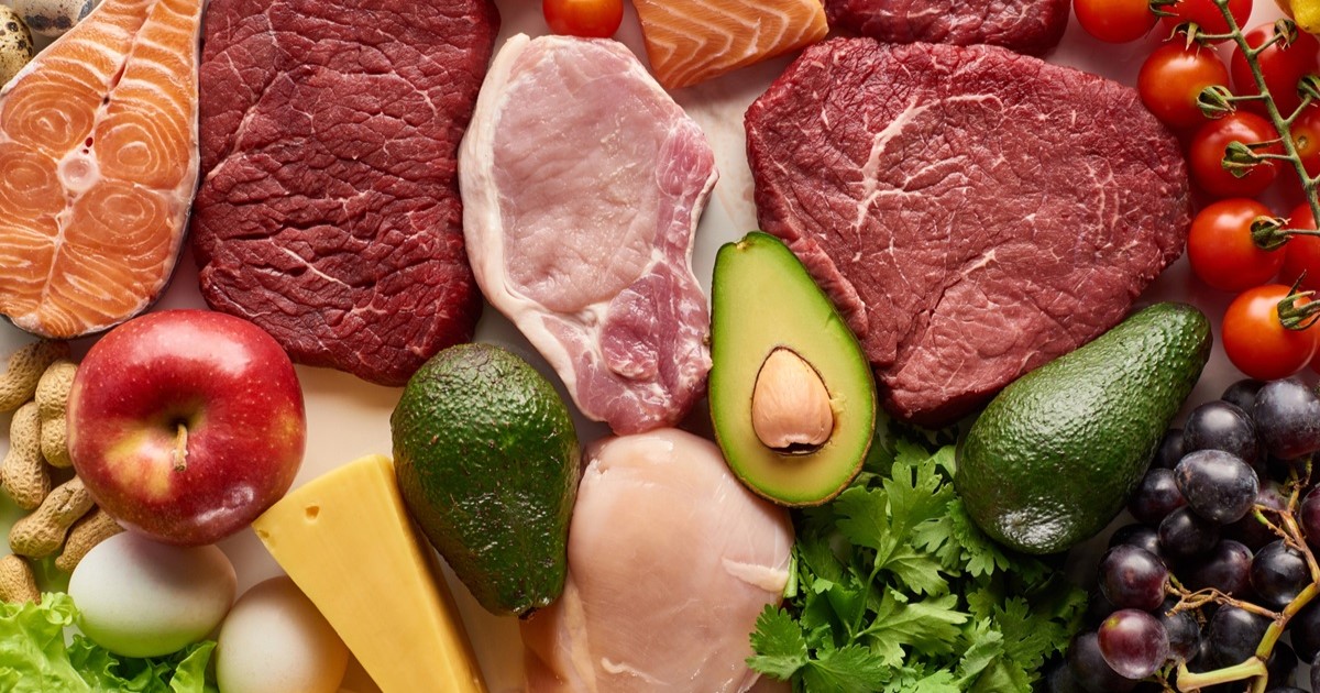 Alimentos frescos y variados, ricos en nutrientes, como carnes, frutas, vegetales, huevos, queso y frutos secos, dispuestos de forma ordenada