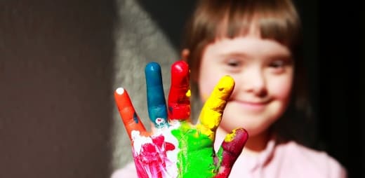 niña con síndrome de Down enseñando su mano pintada.