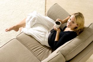 Una joven sentada en un sofá y en su mano un café, síndrome de piernas inquietas