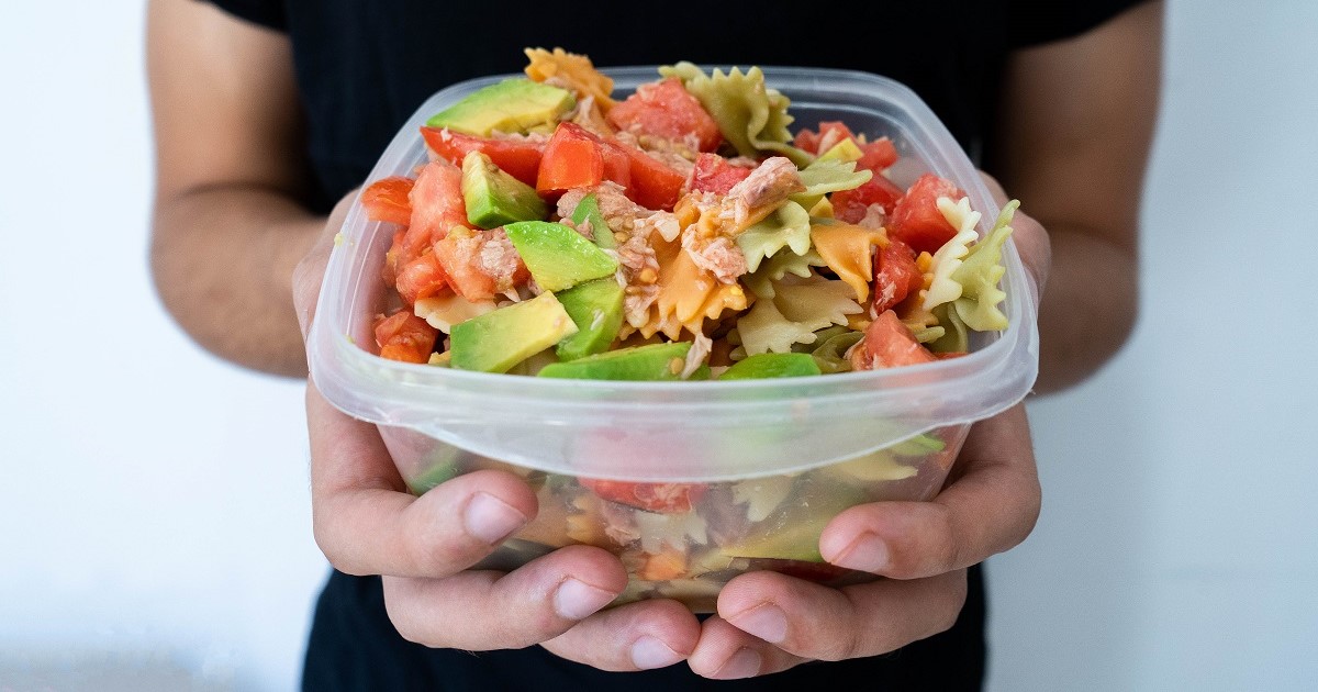 persona con sus dos manos sujeta un tupper de plástico lleno de comida, exactamente ensalada de pasta. Ese tupper de plástico puede presentar sustancias tóxicas en el envase.