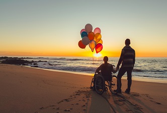 Una pareja viendo amanecer el sol en la playa, una de ellas está en silla de ruedas