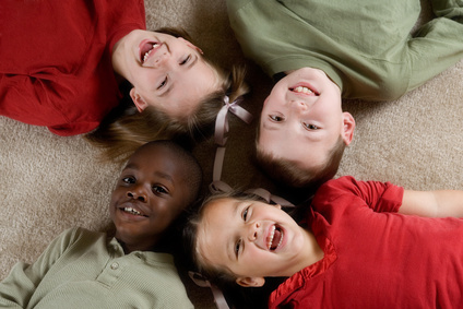 Grupo de cuatro niños sonriendo tumbados en el suelo y juntando sus cabezas, mostrando humor y felicidad