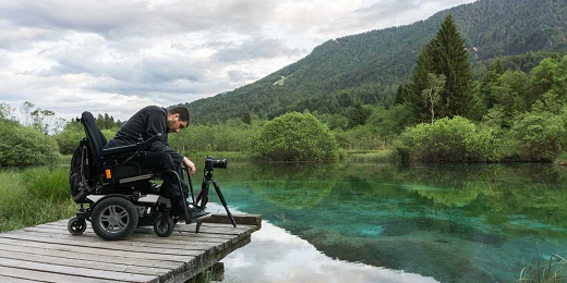 hombre en silla de ruedas haciendo fotos en pasarela de madera de un lago, para reconocimientos Destinos Turísticos Accesibles