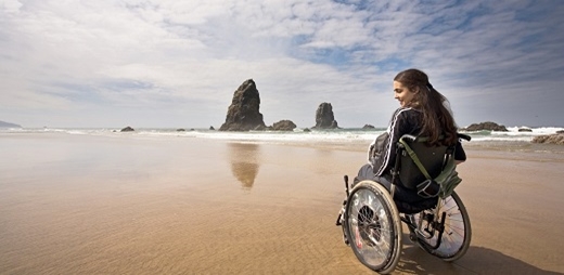 Mujer en silla de ruedas sola en la playa. Soledad no deseada en mujeres con discapacidad