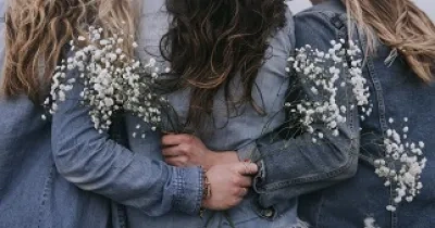 foto de mujeres de espaldas abrazándose, con flores en sus manos