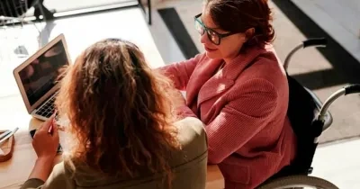 Dos chicas entadas trabajando en una mesa, una de ellas en silla de ruedas