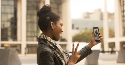 Chica con un dispositivo móvil en la mano haciendo una videollamada, hablando con lengua de signos con su interlocutor-a