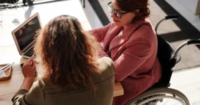 Dos chicas, una en silla de ruedas delante de un portátil