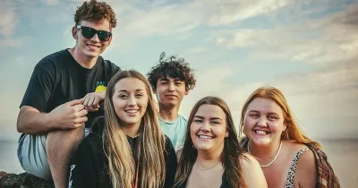 Tres chicas y dos chicos sentados mirando hacia el frente y sonriendo