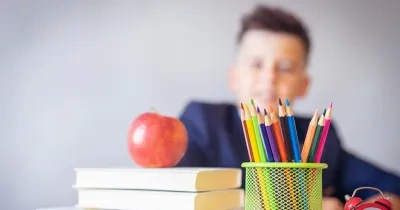 Niño sentado delante de una mesa donde hay lápices de colores, libros y una manzana sobre los libros