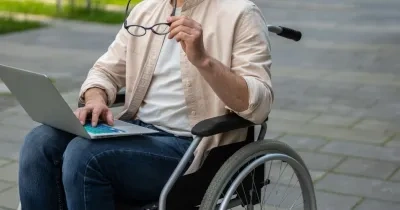 Un estudiante en silla de ruedas consulta su ordenador | Foto de 123RF/zinkevych