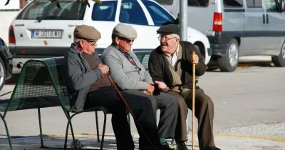 Tres mayores conversan sentados en un banco 
