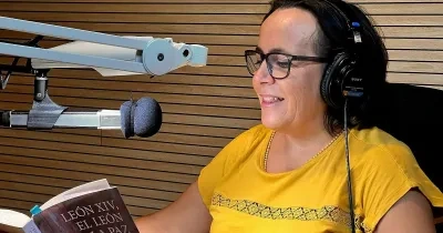 Persona con auriculares sentada en un estudio de grabación frente a un micrófono profesional mientras lee el libro León XIV, el León de la paz, de Almudena Hernández. La imagen muestra la grabación de la versión sonora de la obra, con paneles acústicos de madera al fondo y el ejemplar abierto sobre un atril.