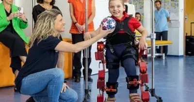 Una mujer entrega un balón a un menor de la Fundación Bobath, miembro de Aspace que utiliza un exoesqueleto pediátrico de pie (Fuente: Marsi Bionics)
