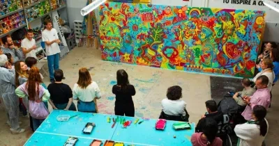 Foto Creación Ilusión con varias personas presenciando la obra, que es un mural grande con mucho colorido.